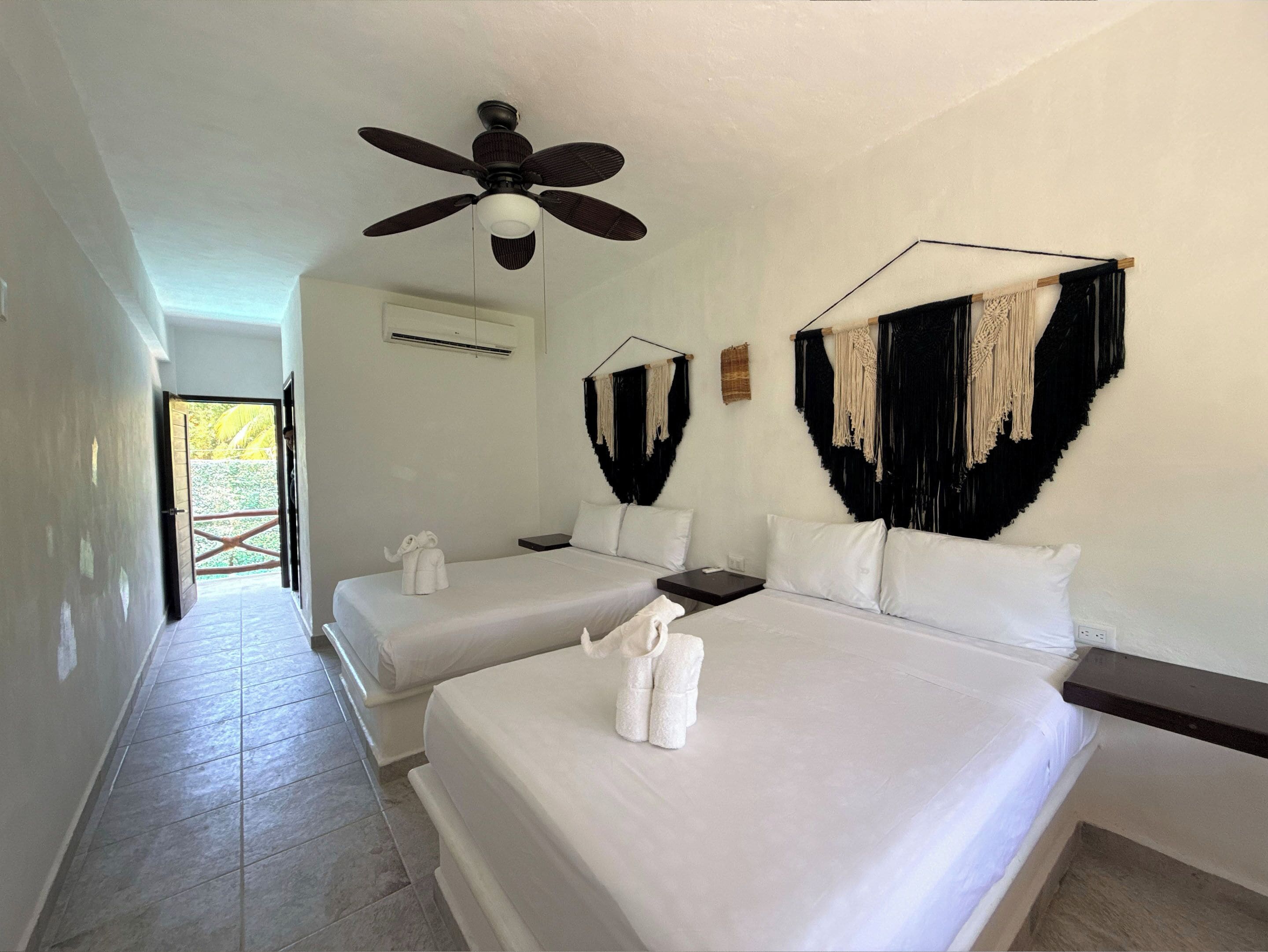 A hotel room with two beds, a ceiling fan, and a view of the outside.