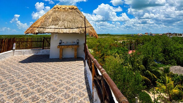 A thatched-roof structure with a sink and a wooden bench, surrounded by a tiled floor and a wooden fence. - Paseo Kuka by ÓOL Hotels (Isla Holbox)
