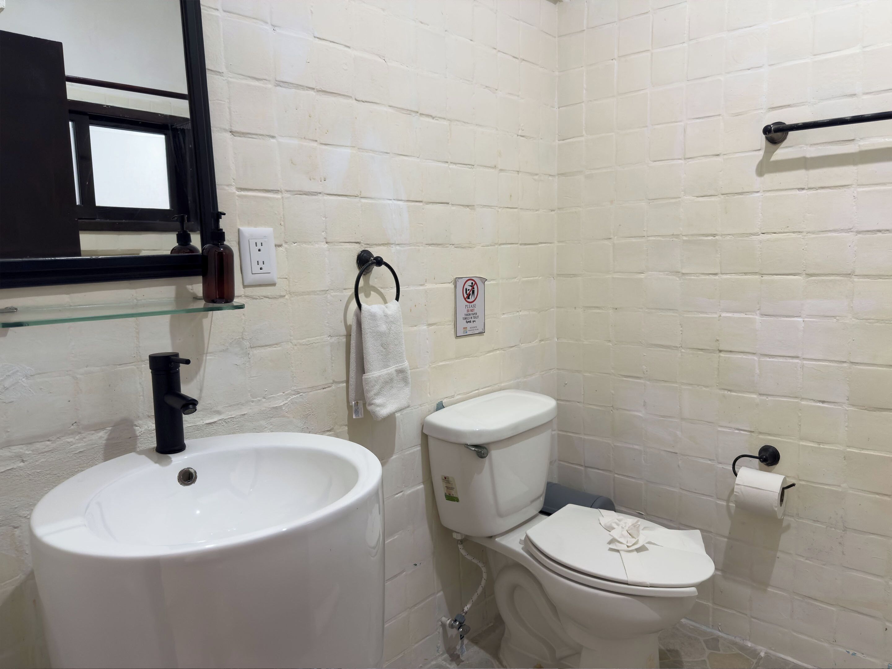 Une salle de bain avec un lavabo blanc, des toilettes et une étagère en verre au-dessus du lavabo.