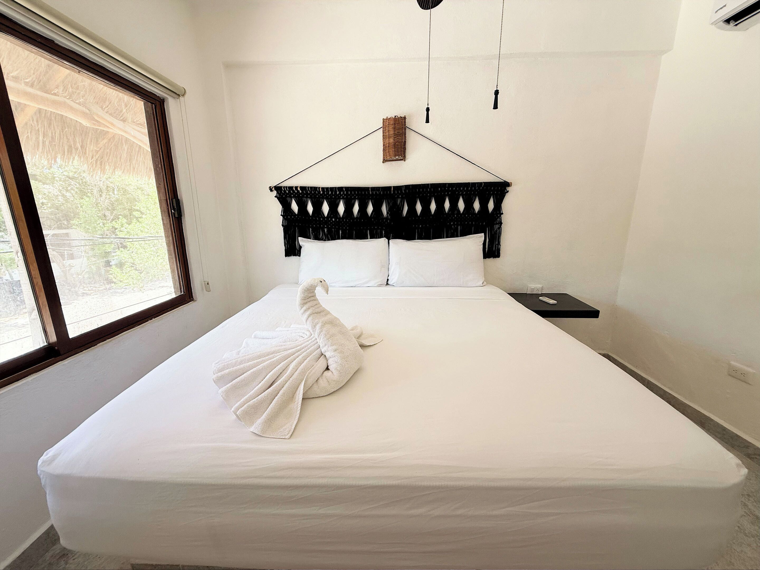 A neatly made bed with a white towel, a black headboard, and a small nightstand with a remote control.