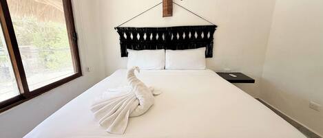 A neatly made bed with a white towel, a black headboard, and a small nightstand with a remote control.