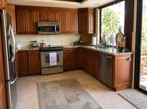 A kitchen with wooden cabinets, stainless steel appliances, a window, and a view of greenery outside. - Condo in Palm Desert, California (Palm Desert)