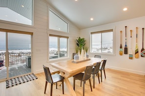 A dining area with a wooden table, four chairs, a plant centerpiece, and a view of the snowy landscape through large windows. - Lake House Sleeps 16 with Views and Amenities (Garden City)