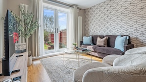 Ett modernt vardagsrum med en soffa, ett soffbord och ett stort fönster med gardiner.