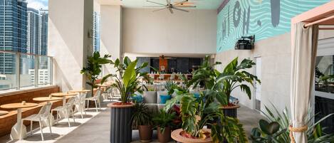 Un bar situé sur le toit d’un immeuble, avec une terrasse, des plantes en pot et une vue sur la ville.