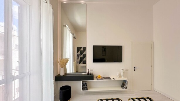 A modern bathroom with a large mirror, a flat-screen TV, and a white door. - Elegant apartment in the center of Matera, 200 meters from the entrance to the Sassi (Matera)