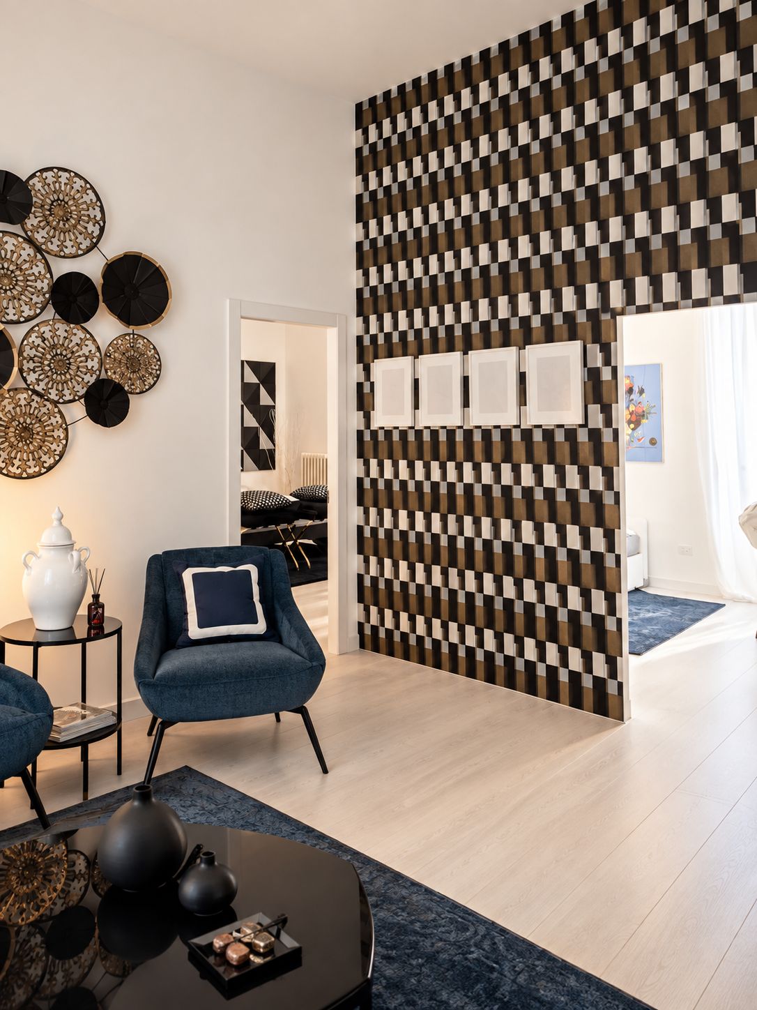 A modern living room with a geometric patterned wall, a blue armchair, a round coffee table, and a decorative wall hanging.
