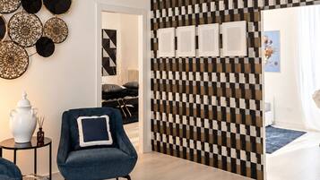 A modern living room with a geometric patterned wall, a blue armchair, a round coffee table, and a decorative wall hanging.