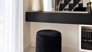 A modern interior with a black console table, a round ottoman with a gold base, and a geometric wall art piece.