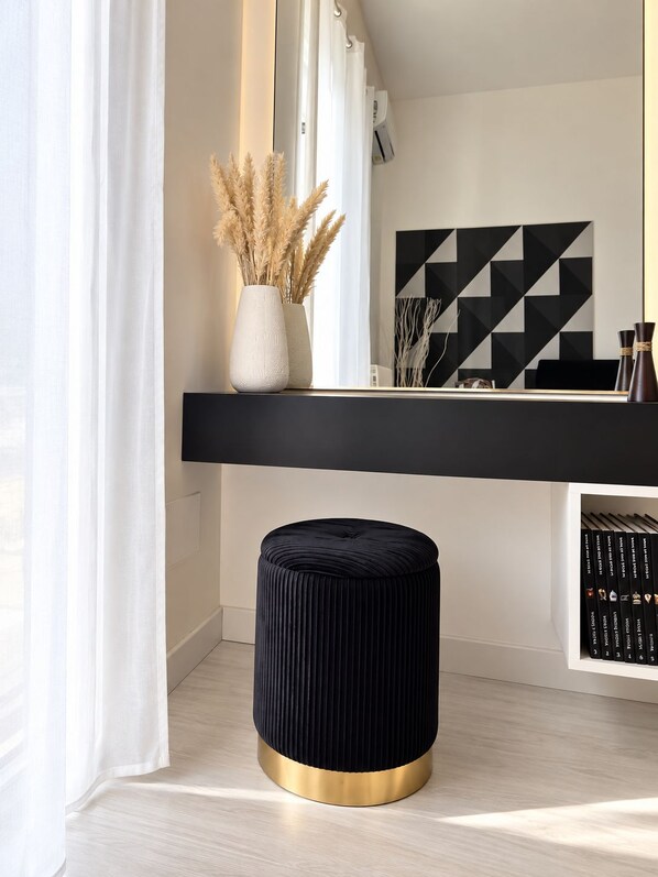 A modern interior with a black console table, a round ottoman with a gold base, and a geometric wall art piece.