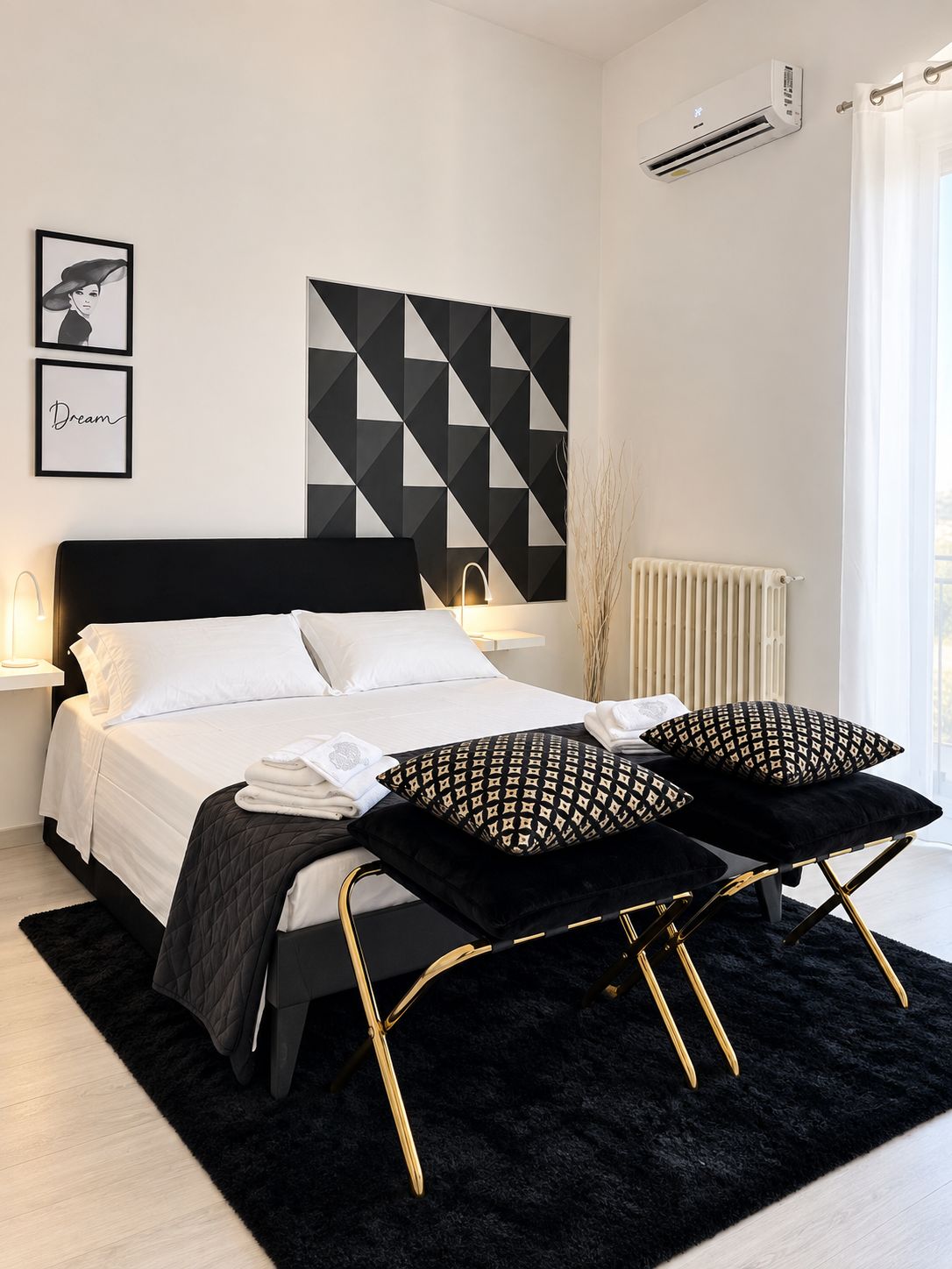 A modern bedroom with a black and white color scheme, a bed with white linens, two black side tables with gold legs, and a geometric wall art piece.