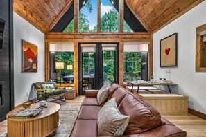 A modern living room with a wooden ceiling, a brown leather sofa, a green armchair, and a dining area with a table and chairs.