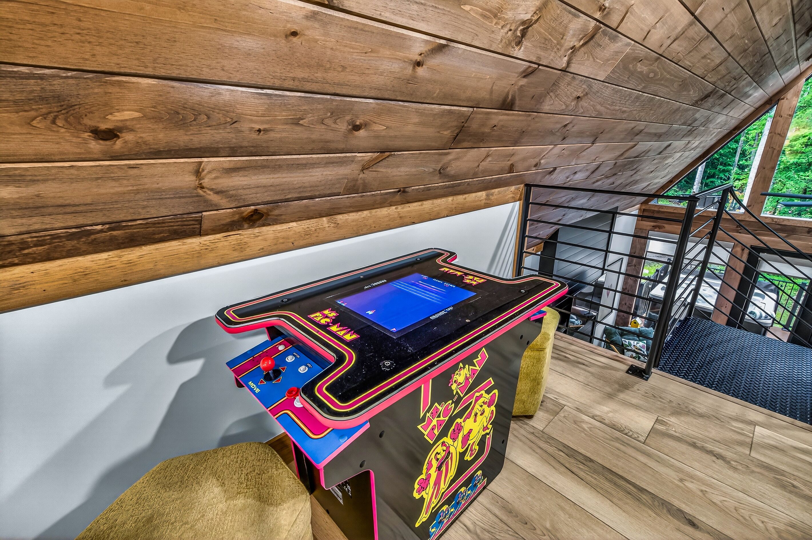 Techo de madera con una mesa y un juego de arcade iluminado con neón.
