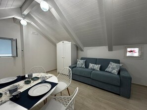 A dining area with a table set for two, a sofa, and a white cabinet. - Room 'Camera Deluxe Amalfi' with Shared Terrace, Wi-Fi and Air Conditioning (Furore)