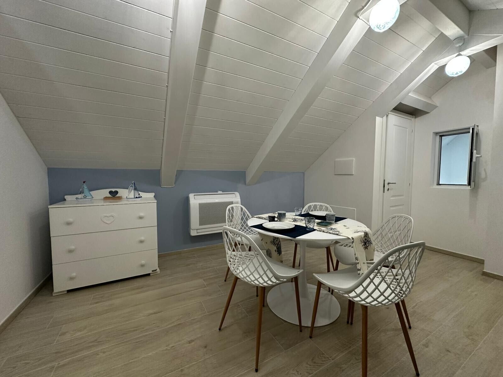 Ein Zimmer mit schrägem Dach, einem weißen Schminktisch, einem Tisch mit Stühlen und einem Fenster.