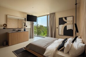 Ein modernes Schlafzimmer mit einem großen Bett, einem Fernseher, einer Holzkommode und einem Fenster mit Vorhängen.