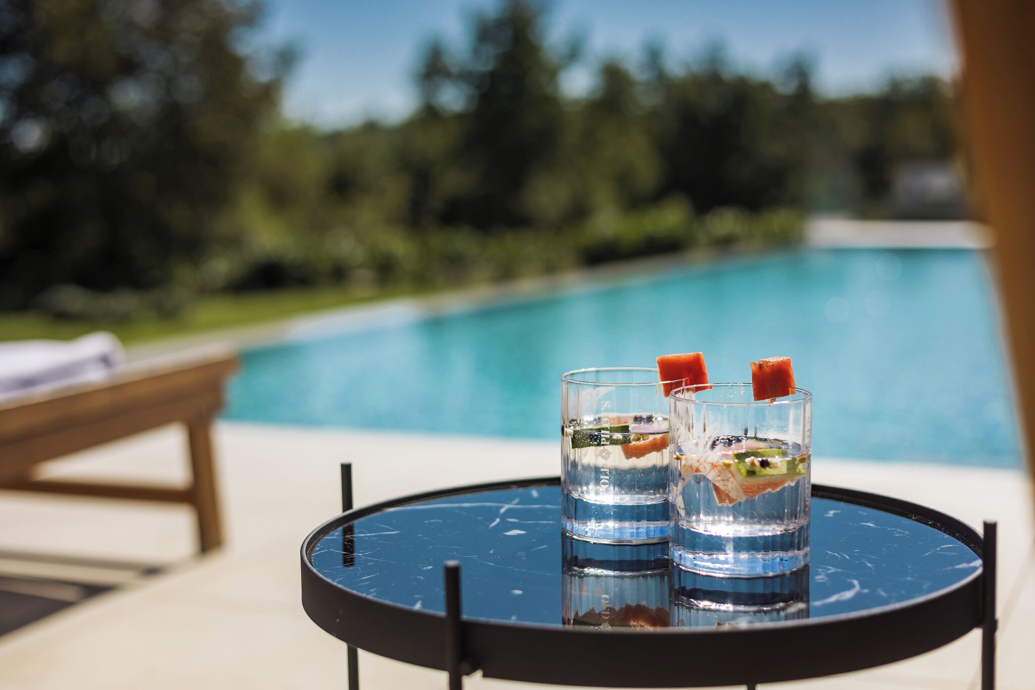 A poolside table with two glasses of water and a slice of watermelon.