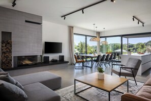 Ein modernes Wohnzimmer mit Kamin, Flachbildfernseher, Essbereich mit Tisch und Stühlen sowie Küchenzeile mit Arbeitsfläche.