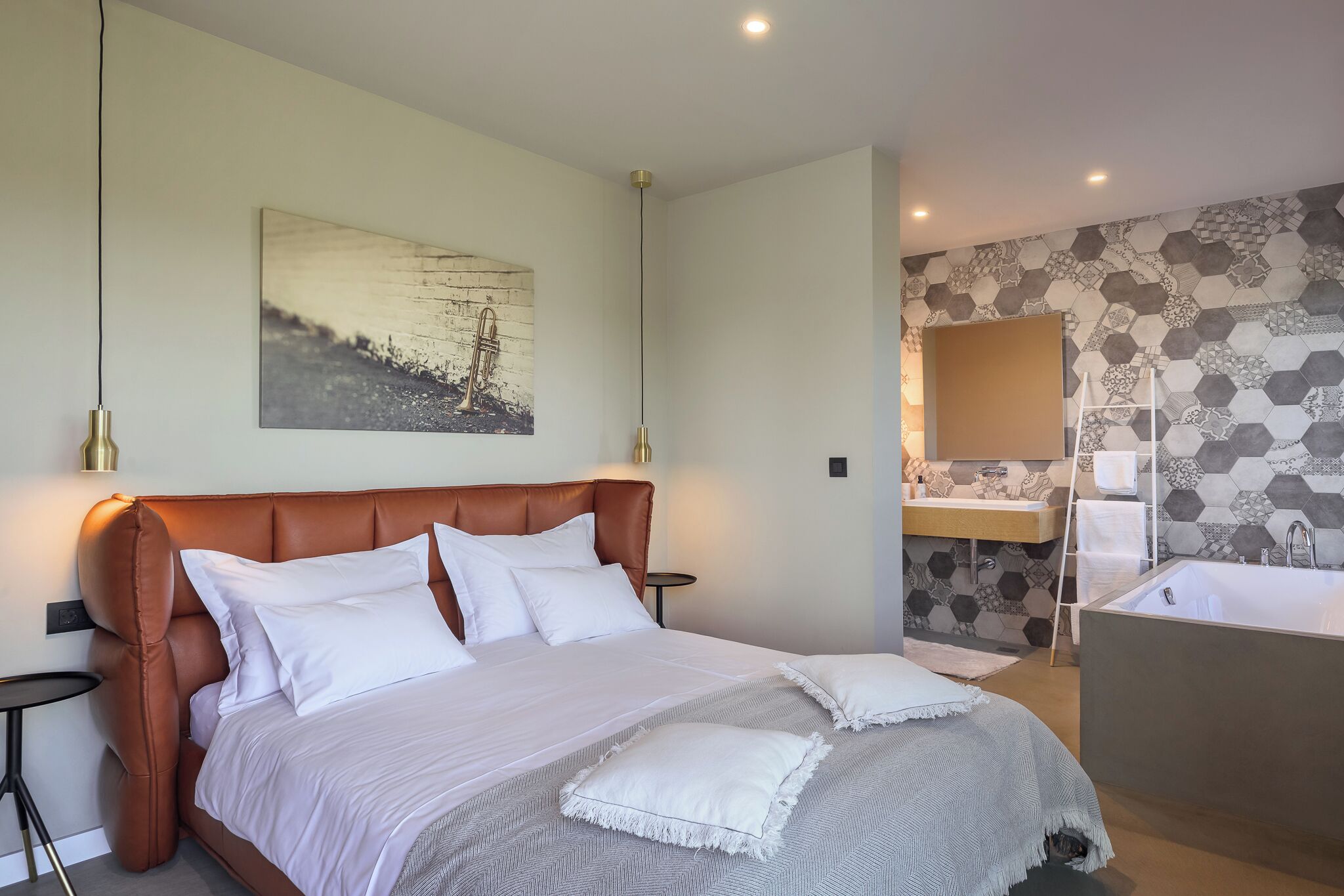 A modern hotel room with a large bed, a bathroom with a bathtub, and a hexagonal patterned wall.