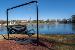 Ein Park mit Schaukeln, einem Gewässer und einer Fontäne.