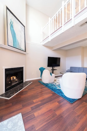 Ein Wohnzimmer mit Kamin, Flachbildfernseher, Sofa und Treppe.