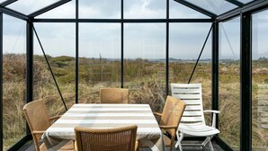 A glass-enclosed dining area with wicker chairs and a table, overlooking a natural landscape.