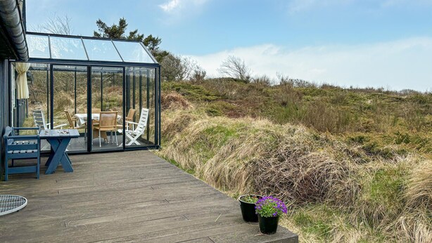 A glass-enclosed outdoor area with a wooden deck, a table with chairs, and potted plants.