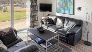 Una sala de estar moderna con un sofá de cuero, una mesa de centro, un televisor de pantalla plana y un cuadro en la pared.