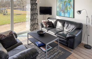 Ein modernes Wohnzimmer mit Ledersofa, Couchtisch, Flachbildfernseher und einem Gemälde an der Wand.