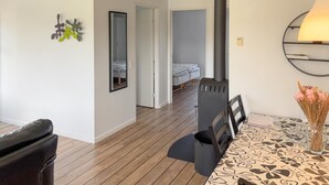Una habitación con una cama, una mesa con mantel estampado, una silla, un radiador negro y un espejo en la pared.