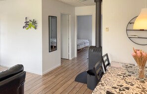 Ein Zimmer mit einem Bett, einem Tisch mit gemustertem Tischlein, einem Stuhl, einem schwarzen Heizgerät und einem Spiegel an der Wand.