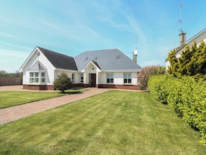 Ein zweigeschossiges Haus mit einem Ziegelweg, der zum Eingang führt, umgeben von gepflegtem Rasen und Hecken.