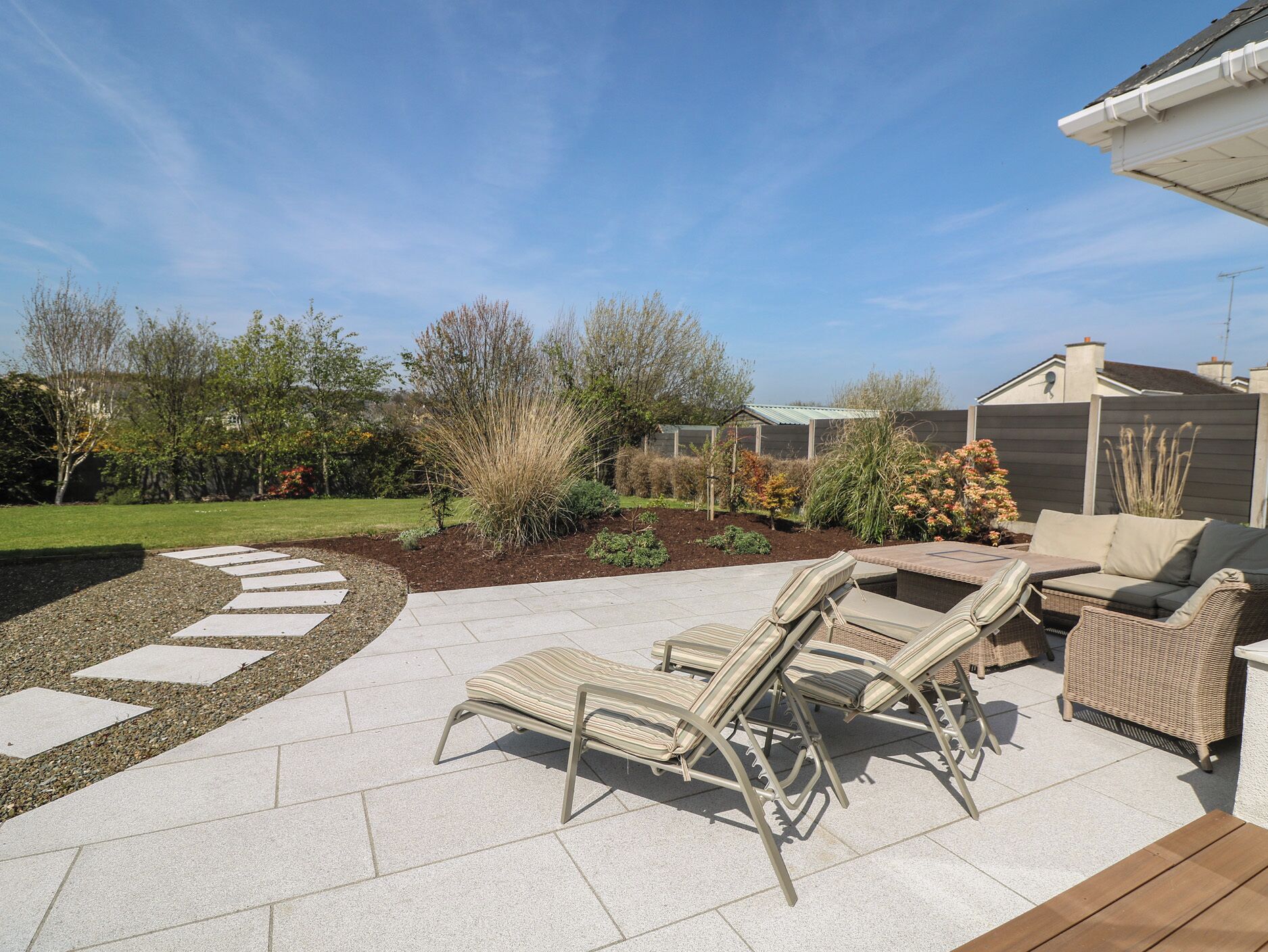 Une terrasse extérieure avec un sol en pierre, des chaises longues et une table en bois.