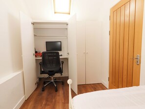 A bedroom with a bed, a wooden wardrobe, a desk with a chair, and a television.