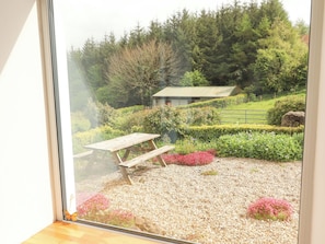 A garden with a wooden picnic table and benches, surrounded by gravel and various plants.