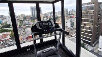 A gym with a treadmill, large windows, and a city view.