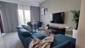 En stue med sofa, fjernsyn, loftventilator og et spiseområde med stole og bord.
