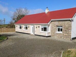 A two-story house with a red roof, stone exterior, and a gravel driveway. - RED HOUSE, pet friendly, with open fire in Carraroe, County Galway (Galway)
