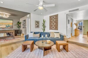 A modern living room with a blue sofa, wooden coffee table, and a ceiling fan.