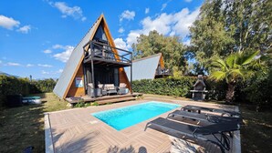 Et moderne A-mønehus med swimmingpool, udendørs møbler og en velplejet have.