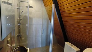 Et moderne badeværelse med en glasafskærmet brusekabine, et hvidt toilet og en stålvask.