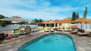 A swimming pool with lounge chairs and umbrellas, a covered seating area, and a house with a tropical theme. - Sleeps 10 • Outdoor Oasis • Heated Pool • Grill (Bradenton)