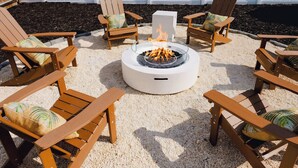 A circular fire pit surrounded by wooden Adirondack chairs with cushions, set on a gravel surface. - Sleeps 10 • Outdoor Oasis • Heated Pool • Grill (Bradenton)