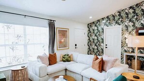 A living room with a sectional sofa, a round coffee table, a wicker chair, a ceiling fan, and a bookshelf. - Sleeps 10 • Outdoor Oasis • Heated Pool • Grill (Bradenton)