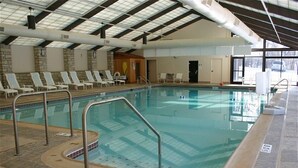 En inomhuspool med kaklade golv, en poolstege och solstolar längs väggarna.
