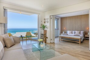 Ein modernes Wohnzimmer mit einem Glastisch, einer Couch, einem Bett und Blick auf den Ozean.
