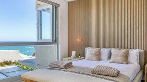 Una camera da letto con un letto grande, un comodino, una paretina laterale e una finestra vista mare, oltre a un pannello di legno al muro.