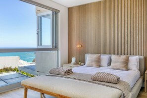 Ein Schlafzimmer mit einem großen Bett, einem Nachttisch, einem Fenster mit Blick auf das Meer und einer Holzwandverkleidung.