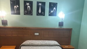 A neatly made bed with a patterned bedspread, two bedside tables with lamps, and four wall-mounted cat-themed artworks. - HOTEL RESTAURANTE LA BARCA (Pedro Munoz)