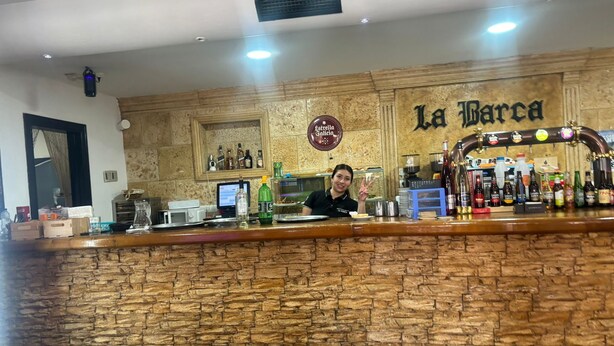 A bar area with a stone wall, a bartender, and a variety of bottles and glasses. - HOTEL RESTAURANTE LA BARCA (Pedro Munoz)